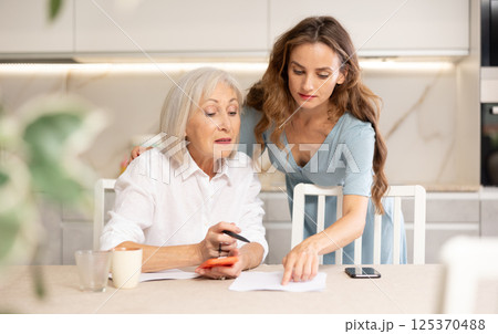Adult woman and elderly woman discussing agreement in kitchen Adult woman and elderly woman discussing agreement in kitchen 125370488
