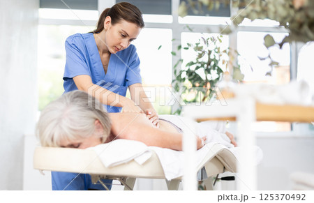 Professional young masseuse doing back massage to elderly woman Professional young masseuse doing back massage to elderly woman 125370492
