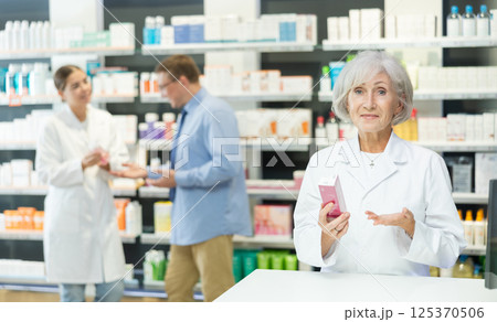 Portrait of elderly female pharmacist offering to buy medicine in pharmacy 125370506