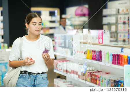 Young girl carefully chooses deodorant and intimate hygiene items in pharmacy 125370516