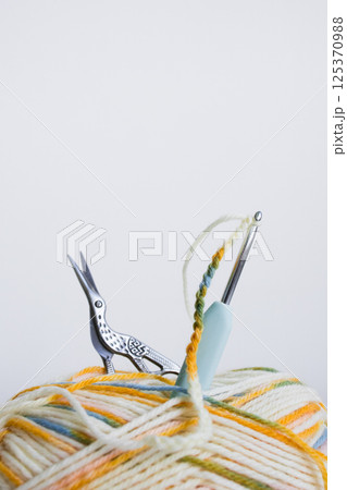 Multicolored yarn ball with crochet hook and scissors on white background 125370988