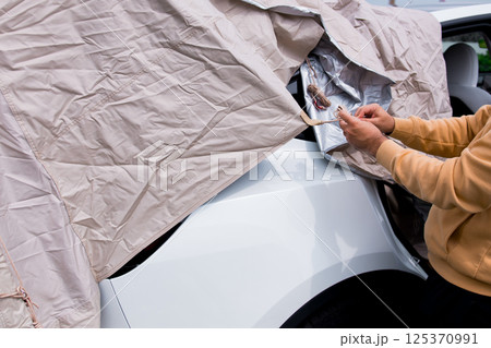 Male uncovering white vehicle under beige cover Male uncovering white vehicle under beige cover 125370991