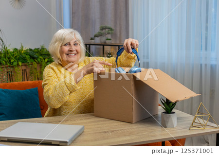 Happy senior woman shopper unpack headphones cardboard box delivery parcel online shopping purchase 125371001