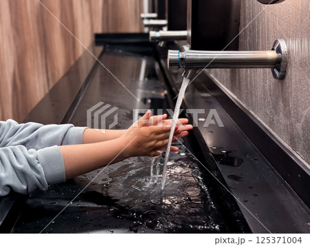 Child washing hands in motion sensor sink in modern restroom 125371004