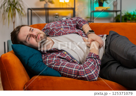 Man lying on sofa feeling sudden strong abdominal stomach ache gastritis problem poisoning diarrhea Man lying on sofa feeling sudden strong abdominal stomach ache gastritis problem poisoning diarrhea 125371079