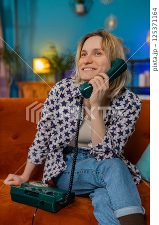 Smiling young woman making wired telephone call conversation with friends sitting on home couch 125371164