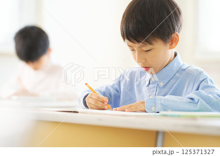 教室で勉強中の男子小学生|真剣な表情で筆記する 教室で勉強中の男子小学生|真剣な表情で筆記する 125371327