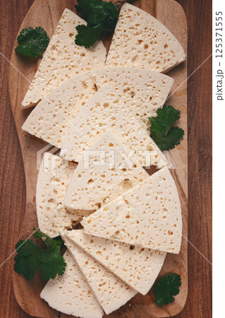 sliced Georgian cheese, factory grade, on a wooden board, top view, sliced Georgian cheese, factory grade, on a wooden board, top view, 125371555