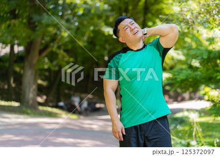 Asian man have shoulder neck joints pain, sport injury concept after running in park outdoors 125372097
