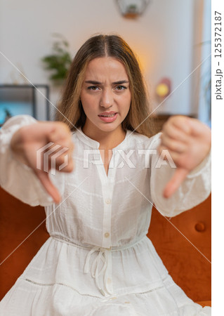Upset young woman showing thumbs down sign gesture, expressing discontent sitting on sofa at home Upset young woman showing thumbs down sign gesture, expressing discontent sitting on sofa at home 125372187