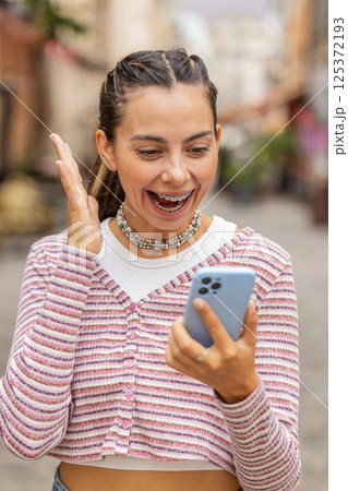 Young woman use mobile smartphone celebrating win good message news outdoors on urban city street 125372193