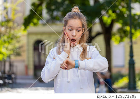 Young woman worrying to be punctual, with anxiety checking time on watch, running late to transport 125372208