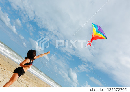 low angle view of small girl flying a kite on the beach 125372765