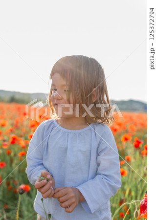 portrait of little child standing in front of big field of poppies 125372794