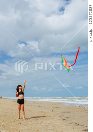 wide angle view of small girl flying a kite on the beach 125372887