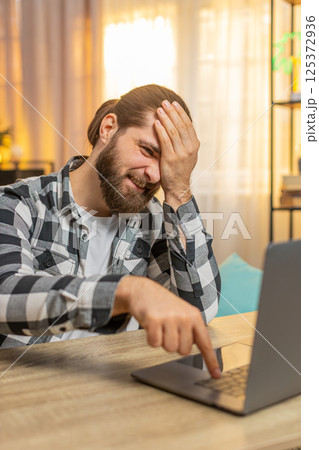Young man working at home, laptop frustration, facepalm, critical error found, annoyed muttering Young man working at home, laptop frustration, facepalm, critical error found, annoyed muttering 125372936