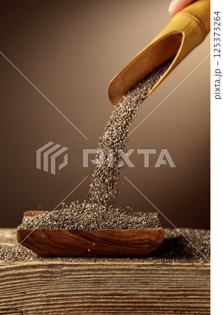 Chia seeds is poured into a wooden bowl. 125373264