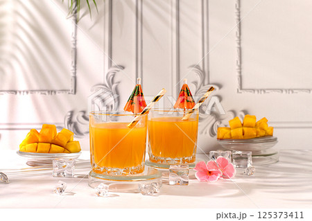 Summer party concept and Detox diet, Modern still life with tropical fruits. Homemade cocktail, juice or lemonade with mango slices and ice on sunny kitchen table. Restaurant menu Summer party concept and Detox diet, Modern still life with tropical fruits. Homemade cocktail, juice or lemonade with mango slices and ice on sunny kitchen table. Restaurant menu 125373411