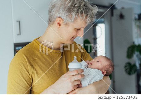 Happy Young father carrying and feeding his newborn baby with formula milk bottle. Food Adoption. Child health and skin care concept. Problems with breastfeeding, food allergy, gassy stomach, colics Happy Young father carrying and feeding his newborn baby with formula milk bottle. Food Adoption. Child health and skin care concept. Problems with breastfeeding, food allergy, gassy stomach, colics 125373435