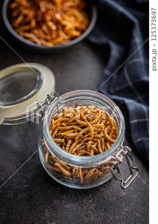 Dried salted worms. Roasted mealworms in jar on black table. Dried salted worms. Roasted mealworms in jar on black table. 125373697