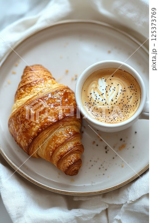 Delicious cappuccino with croissants served on a plate with warm lighting 125373769
