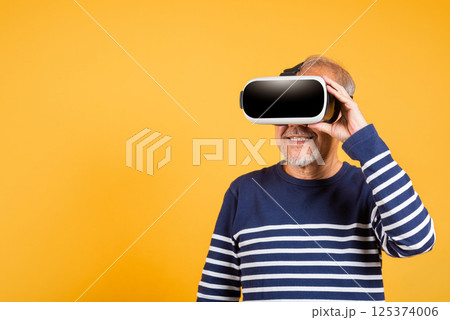 Portrait Asian smiling old man holding in a virtual reality glasses headset studio shot isolated yellow background, Excited happy senior man pensioner using VR play simulation game 125374006