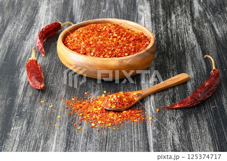Wooden bowl with crushed chili pepper and fresh red chili pepper on old table. Selective focus. 125374717