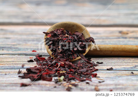 Karkade tea. Hibiscus tea leaves in wooden spoon isolated on wooden background. File contains clipping path. Top view. Selective focus. Karkade tea. Hibiscus tea leaves in wooden spoon isolated on wooden background. File contains clipping path. Top view. Selective focus. 125374769