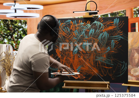 Painter applies watercolor paints to a canvas with his fingers, creating a stunning piece of fine art. Using vibrant colors and finger painting techniques to reflect his creativity and inspiration. 125375584
