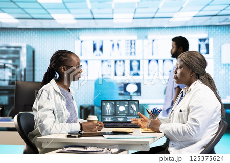 African american medic practitioner discuss with a girl about health care concerns, utilizing medical data and tech equipment to enhance treatment and prevention. Clinic examination. African american medic practitioner discuss with a girl about health care concerns, utilizing medical data and tech equipment to enhance treatment and prevention. Clinic examination. 125375624