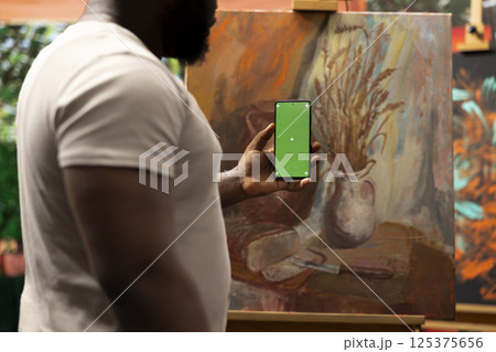 Male artist feeling inspired to paint a new artwork and holding phone with isolated display, thinking about a new painting technique in art and craft atelier. Working with motivation and creativity. Male artist feeling inspired to paint a new artwork and holding phone with isolated display, thinking about a new painting technique in art and craft atelier. Working with motivation and creativity. 125375656