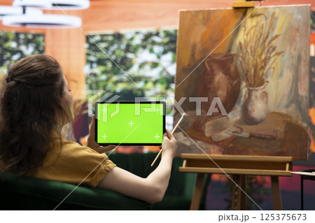 Painter admiring her creative masterpiece in art studio next to green screen, finishing her oil paint mixed with watercolor artwork. Creative artist enjoying quality time in her atelier. 125375673