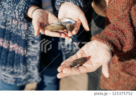 Seashells in hands, close-up. Young carefree couple in love throwing pebbles, shells, stones into sea outdoors. Fun family game together. High quality photo Seashells in hands, close-up. Young carefree couple in love throwing pebbles, shells, stones into sea outdoors. Fun family game together. High quality photo 125375752
