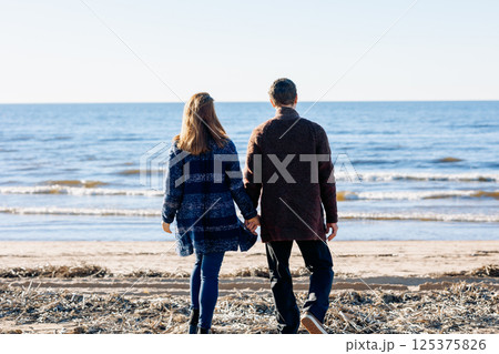 Loving couple walks on beach along sea on sunny autumn day. Weekend and lifestyle concept. Back view. High quality photo 125375826