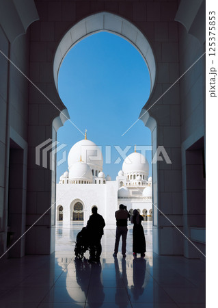 View of Sheikh Zayed Grand Mosque in Abu Dhabi made of white marble with flowers made of precious stones in design and beautiful reflections. Silhouettes of tourists admiring beauty of art. Vertical 125375853