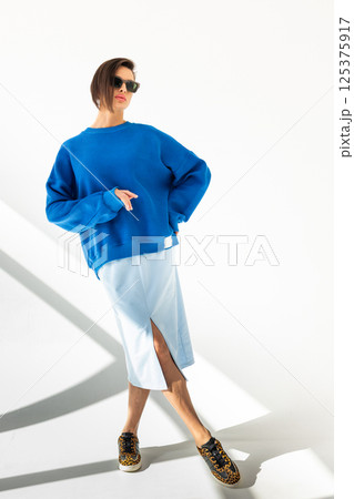 Elegant woman in blue sweatshirt and light blue skirt on white background. Fashionable female style. Studio photography. Vertical photo. High quality photo 125375917