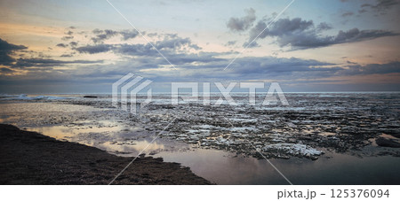 Spring landscape. Panoramic view of beautiful dawn on bay. Cumulus clouds over water in bright light. Ice, snow and rocks on coastline. Rising rays of sun are reflected in sea. High quality photo Spring landscape. Panoramic view of beautiful dawn on bay. Cumulus clouds over water in bright light. Ice, snow and rocks on coastline. Rising rays of sun are reflected in sea. High quality photo 125376094