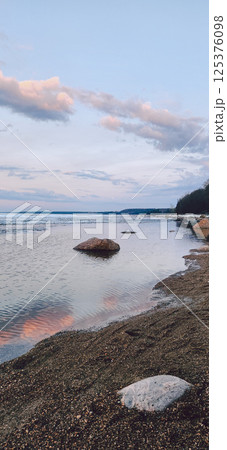 Spring landscape. Panoramic view of beautiful dawn on bay. Cumulus clouds over water in bright light. Ice, snow and rocks on coastline. Rising rays of sun are reflected in sea. Vertical photo. Spring landscape. Panoramic view of beautiful dawn on bay. Cumulus clouds over water in bright light. Ice, snow and rocks on coastline. Rising rays of sun are reflected in sea. Vertical photo. 125376098