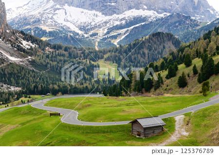Serene mountain landscape with winding road and cabin amidst lush greenery near Valley of Funes at Dolomites, Italy 125376789