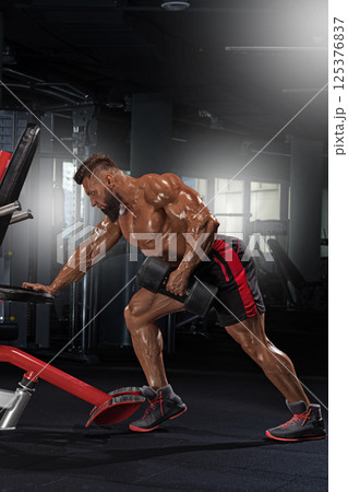 muscular individual engages in weightlifting well equipped gym. Focused on building strength he performs exercise dumbbells showcasing determination and dedication. 125376837