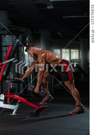 dedicated athlete performs weighted exercise using dumbbells in sleek gym setting. environment features gym equipment and mirrors enhancing focus on fitness. 125376838