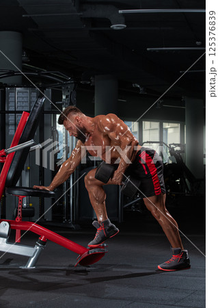 athletic man is engaged in strength training focusing on his upper body using gym equipment. well lit gym features various fitness tools enhancing workout ambiance. 125376839