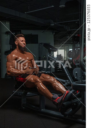 muscular man performs workout on rowing machine in modern gym setting. focus is on his effort and dedication improving physical fitness and strength. 125376855