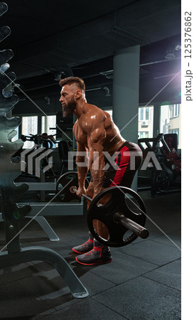 muscular person executes deadlift in well lit gym filled exercise equipment. focus is on strength training and fitness. 125376862