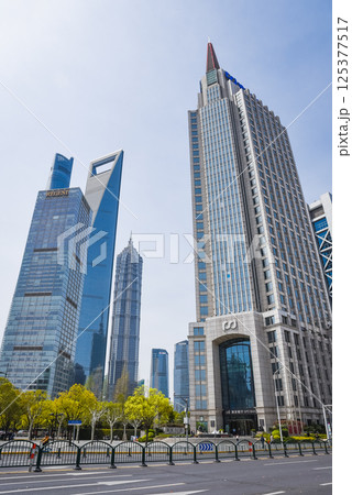 The Shanghai World Financial Center stands tall among Pudongs skyscrapers, its distinctive trapezoid aperture piercing the clear daylight sky. The Shanghai World Financial Center stands tall among Pudongs skyscrapers, its distinctive trapezoid aperture piercing the clear daylight sky. 125377517
