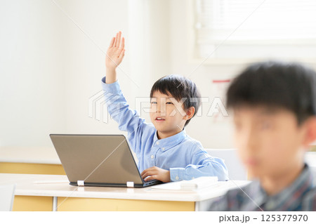 ノートパソコンを開いて手を挙げる小学生の男の子 125377970