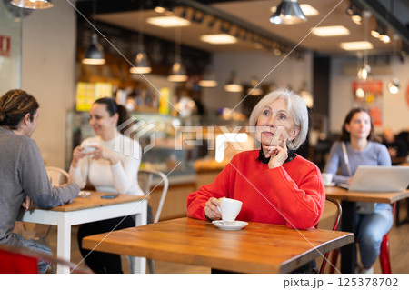 Senior woman whiles away time and waits for meeting in chain cafe 125378702