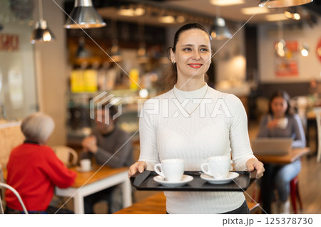 Woman visitor in self-service cafeteria carries tray with two cups of coffee. Woman visitor in self-service cafeteria carries tray with two cups of coffee. 125378730