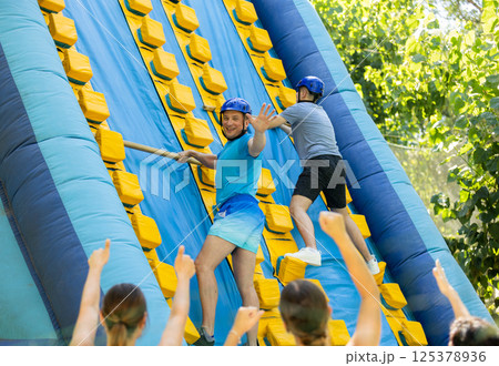 Happy active man climbing on inflatable castle with wooden sticks 125378936