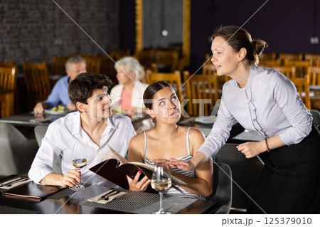 Waitress helps to sort out menu, choose original dish to young married couple 125379010